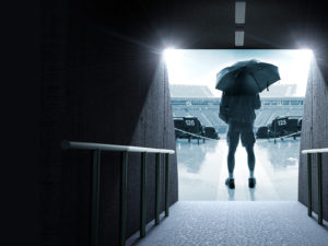 A man standing at the end of a tunnel that leads to an empty stadium. The stadium is empty.